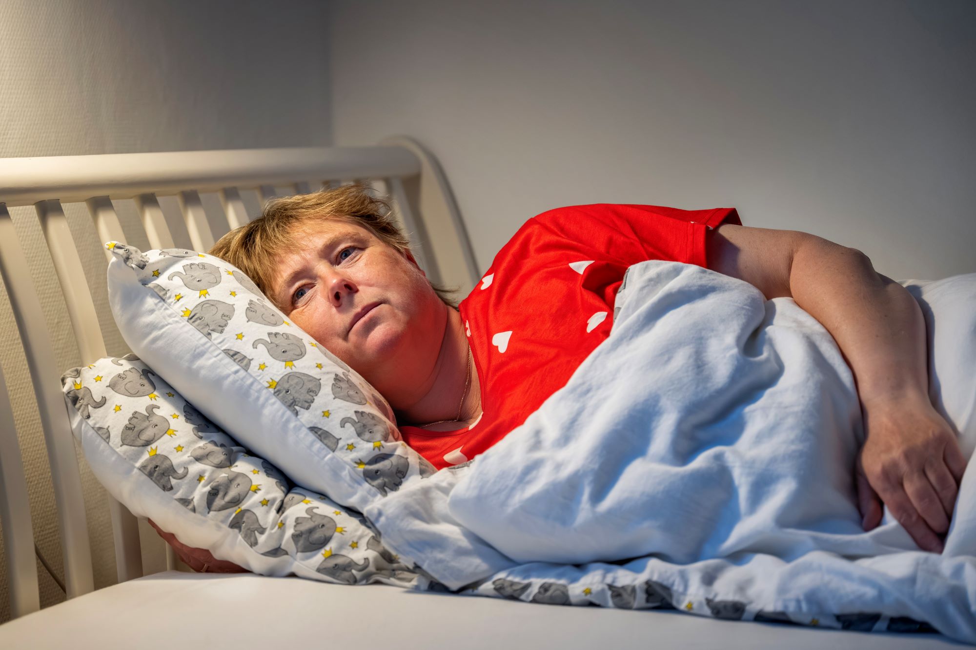 Kvinde ligger på siden i en seng med åbne øjne.