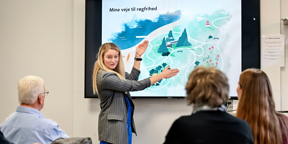 Sundhedspilot Marie Bøgstrup Sørensen står foran skærm og underviser deltagere.