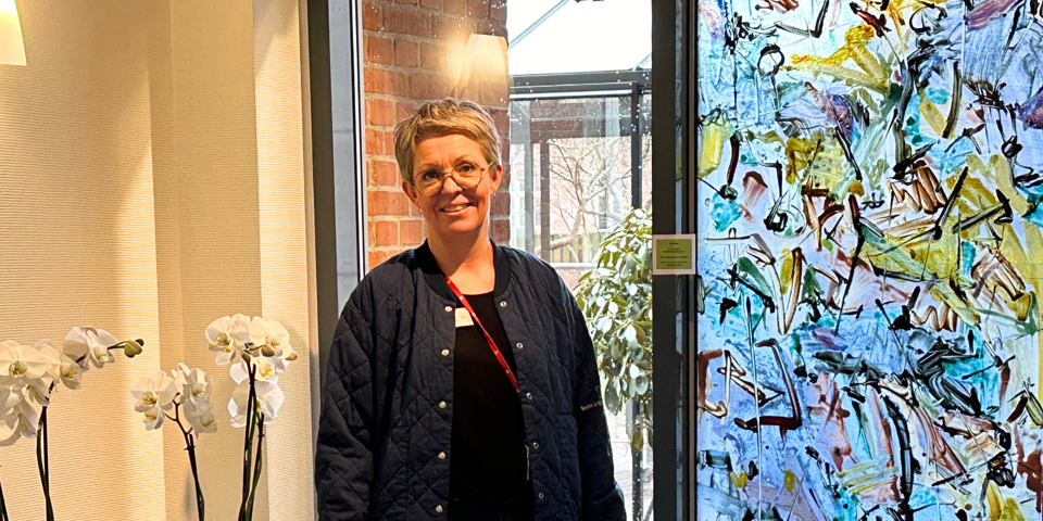 Foto af Pernille Tandrup Nielsen, der er kvalitets- og udviklingssygeplejerske på Hospice Sydvestjylland. Pernille står foran en blå glasmosaik