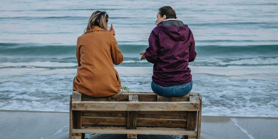 To kvinder sidder sammen ved vandet og snakker sammen 
