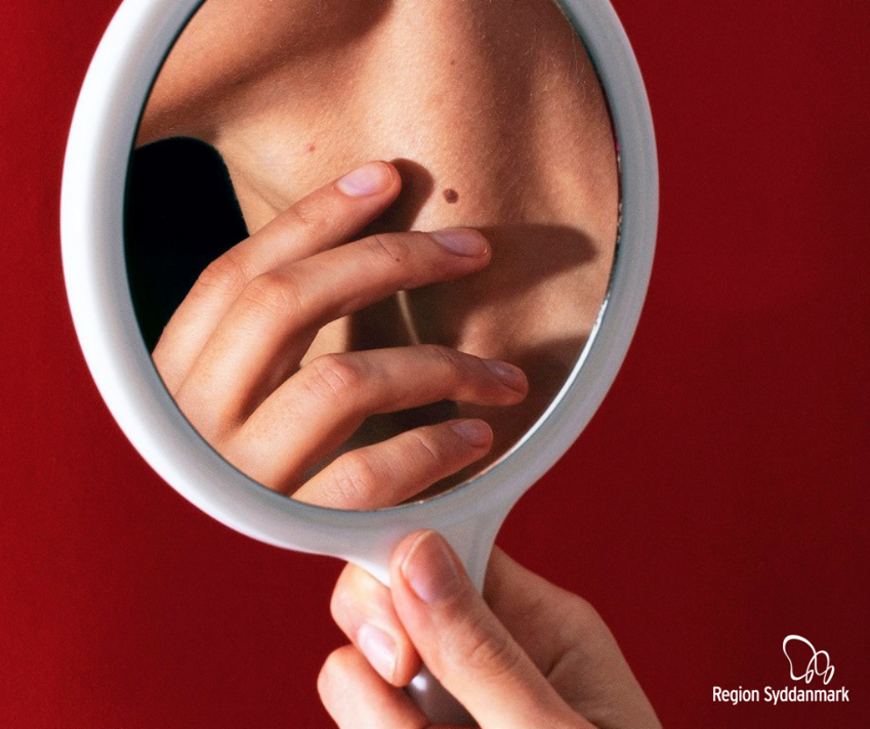 Kvinde tjekker modermærker i et håndspejl