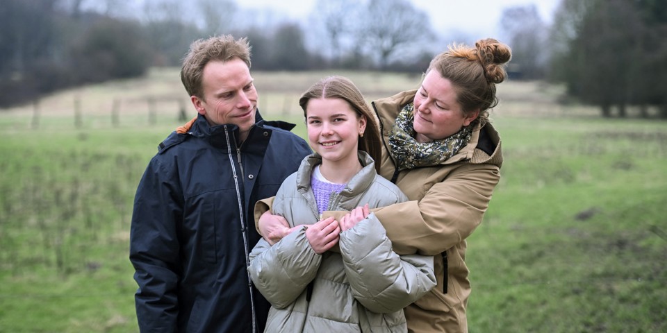 Forældre med 13-årig datter mellem sig fotograferet ude i naturen.