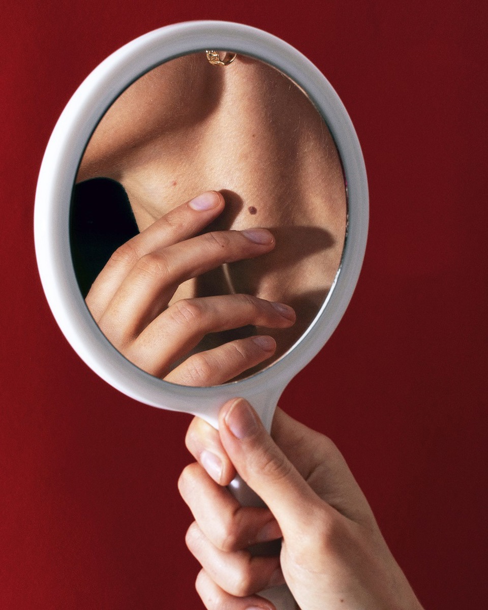 Kvinde tjekker et modermærke i et håndspejl