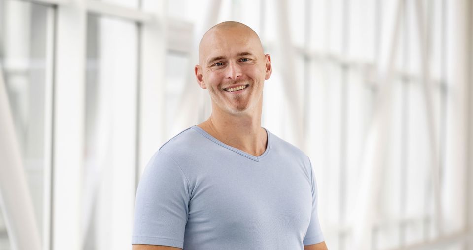 Mandlig portør i lyseblå t-shirt fotograferet på glasgang på Sygehus Lillebælt.