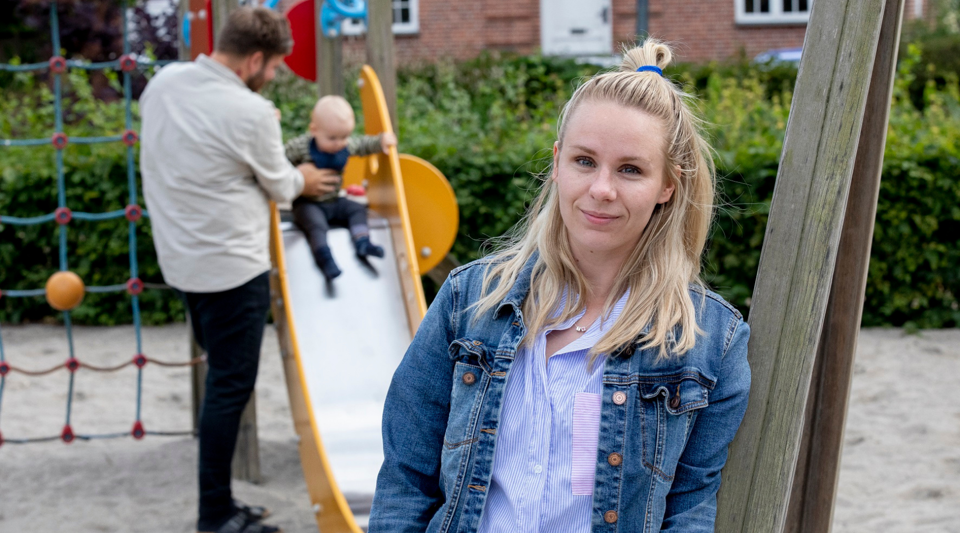 Lisa står i forgrunden, imens hendes mand og søn leger på en rutsjebane i baggrunden.