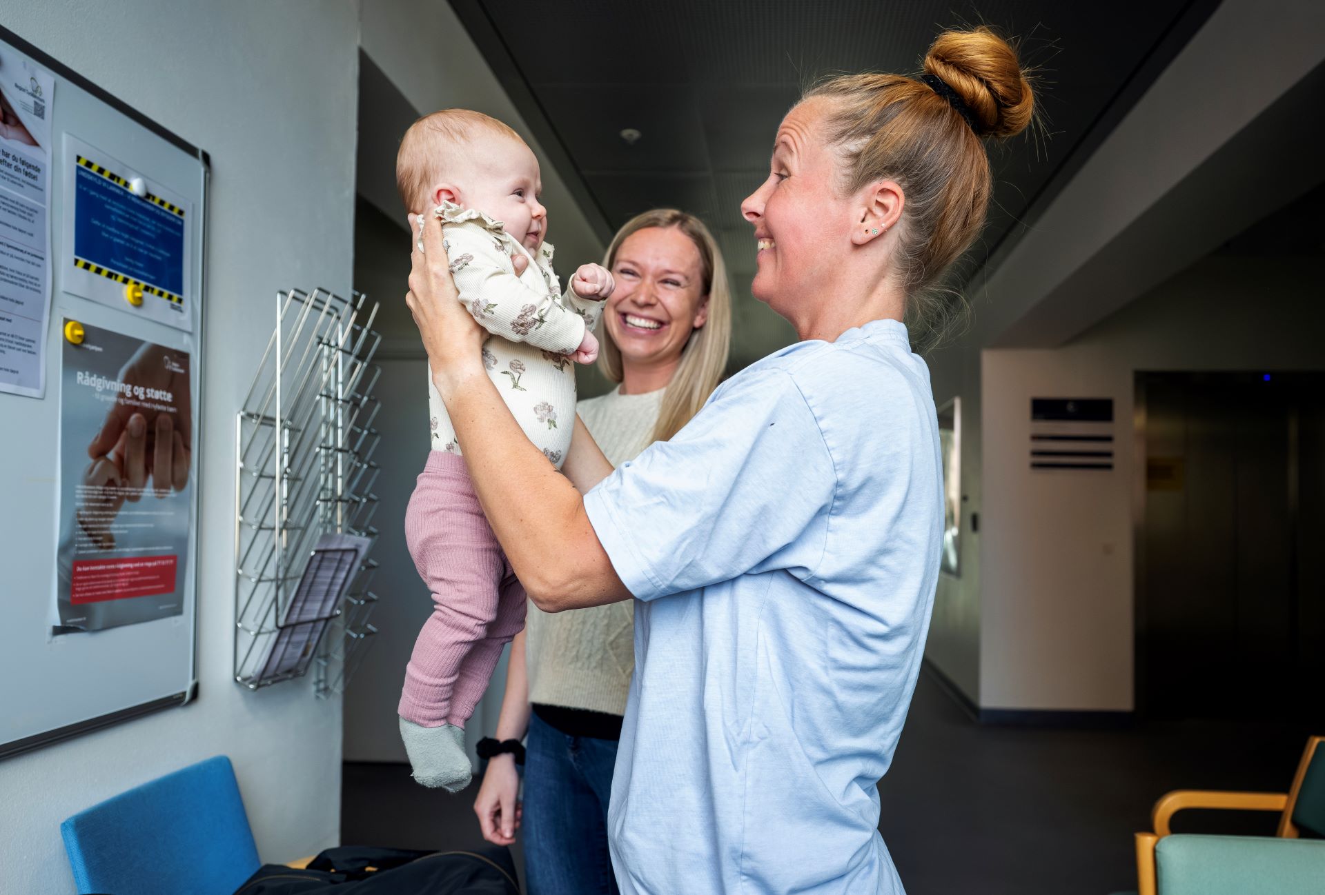 Jordemoder løfter lille pige op foran sit ansigt og de smiler begge.