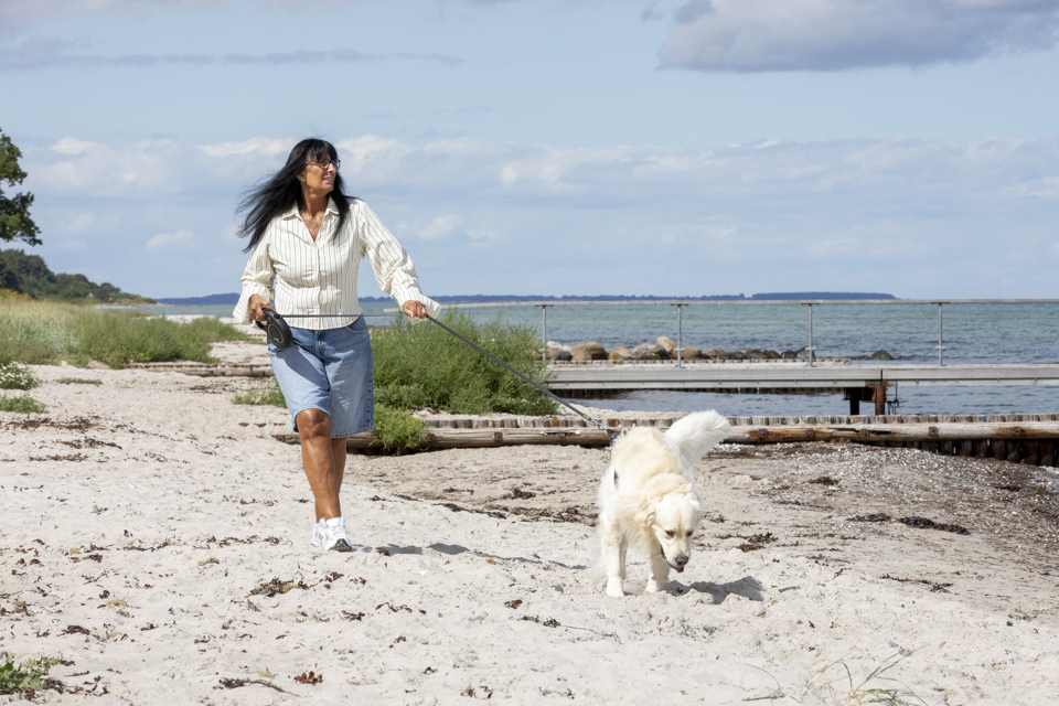 Kvinde går tur med sin hund ved stranden.