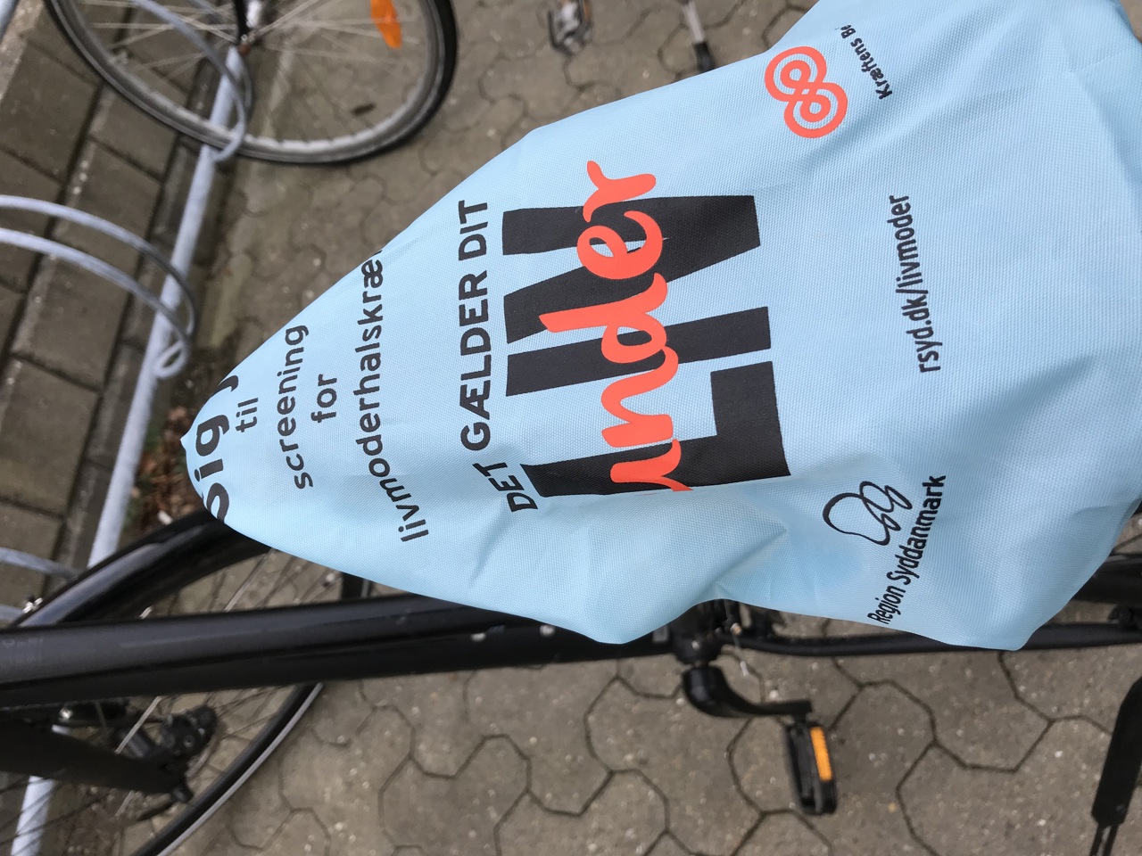 Hvis du har en damecykel, som du stiller ved en banegård eller et andet sted, hvor der står mange cykler, får du måske snart en hilsen fra Kræftens Bekæmpelse og Region Syddanmark. Hilsenen består af et lyseblåt sadelovertræk med teksten ”Sig ja til screening for livmoderhalskræft – det gælder dit (under)liv.”