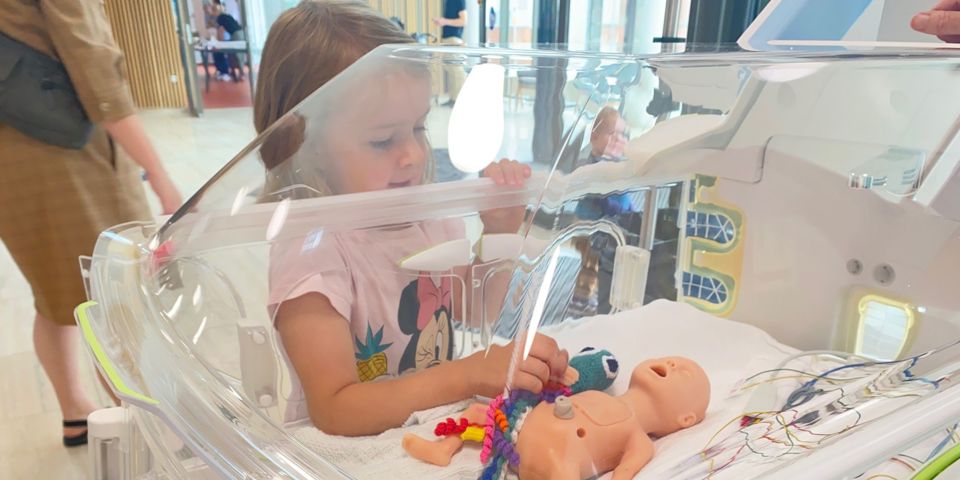 En pige undersøger en babydukke, som ligger i kuvøse