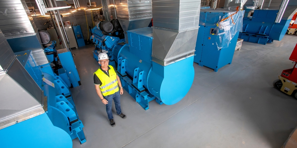 Mand med sikkerhedshjelm og vest står foran nødstrømsanlæg