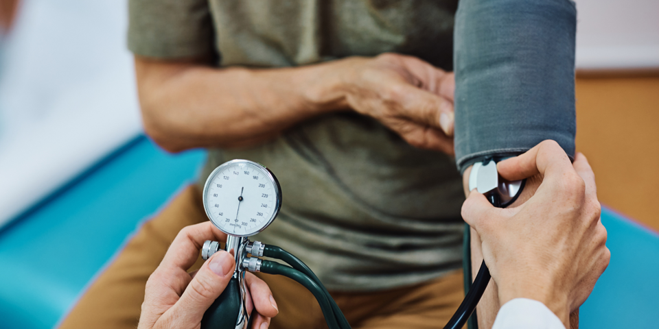 Person sidder på briks og får målt sit blodtryk af læge